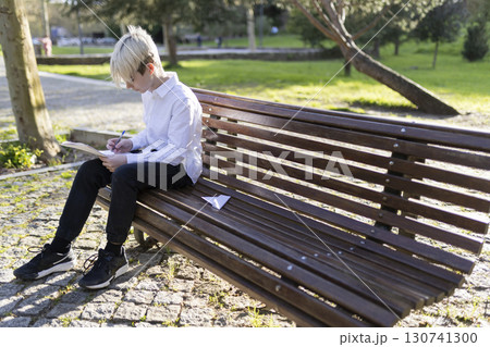 Young student doing homework on park bench after school Young student doing homework on park bench after school 130741300
