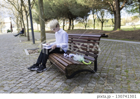 Young student studying on park bench with folded umbrella Young student studying on park bench with folded umbrella 130741301