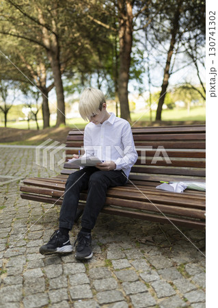 Young student studying outdoors, taking notes on a park bench 130741302
