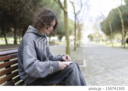 Young man reading a letter on a park bench 130741305