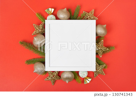 White frame with Christmas tree ornaments and green Christmas tree branches on a red background for text, greetings, offers, discounts, and advertisements. White frame with Christmas tree ornaments and green Christmas tree branches on a red background for text, greetings, offers, discounts, and advertisements. 130741343