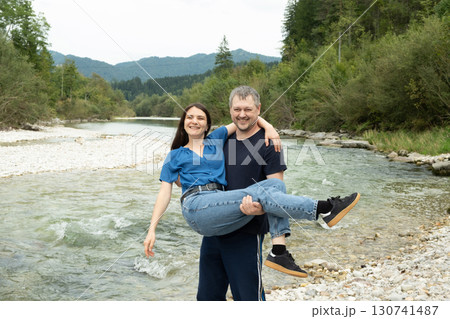 Happy young married couple, husband holding wife in arms in nature near river. Happy young married couple, husband holding wife in arms in nature near river. 130741487