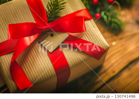 Beautifully wrapped Christmas gift with red ribbon on rustic wooden surface, creating warm and inviting holiday atmosphere. Ideal for Christmas card, seasonal promotions, or gift ideas Beautifully wrapped Christmas gift with red ribbon on rustic wooden surface, creating warm and inviting holiday atmosphere. Ideal for Christmas card, seasonal promotions, or gift ideas 130741496