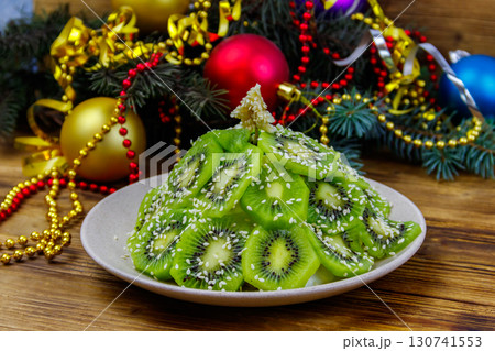 Christmas tree shaped fruit salad and Christmas decorations on wooden table. Creative idea for Christmas and New Year festive desserts. Funny food idea for kids Christmas tree shaped fruit salad and Christmas decorations on wooden table. Creative idea for Christmas and New Year festive desserts. Funny food idea for kids 130741553