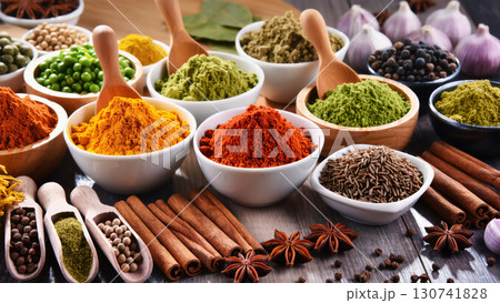 Various colorful ground and whole spices in bowls with herbs, cinnamon, garlic and peppercorns on rustic wooden table 130741828
