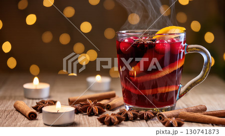 Christmas mulled wine in glass mug with spices, citrus, and cranberries on wooden table with candles and glowing festive lights Christmas mulled wine in glass mug with spices, citrus, and cranberries on wooden table with candles and glowing festive lights 130741873