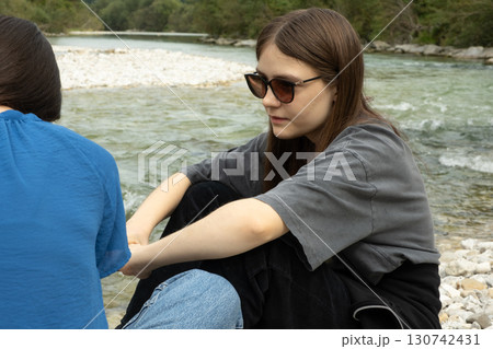 Friends are sitting on the bank of the river and talking. Communication of people 130742431