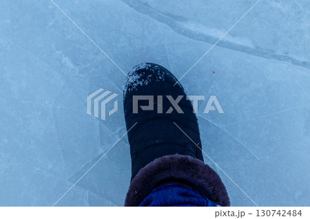 Foot standing on cracked natural lake ice texture. Concept of danger exit to badly frozen water 130742484
