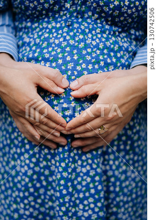 Pregnant couple holding hands on belly in heart shape, celebrating new life 130742506
