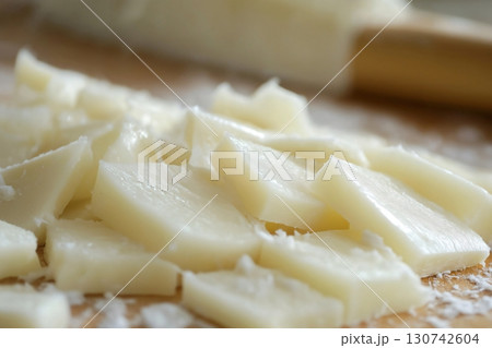 Slicing a block of fresh mozzarella cheese into cubes on a wooden cutting board Slicing a block of fresh mozzarella cheese into cubes on a wooden cutting board 130742604