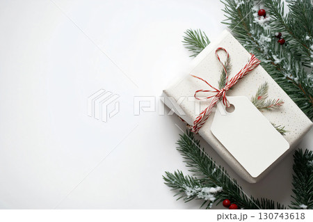 Christmas gift wrapped in white paper with a blank tag is laying on a white surface with fir branches around Christmas gift wrapped in white paper with a blank tag is laying on a white surface with fir branches around 130743618
