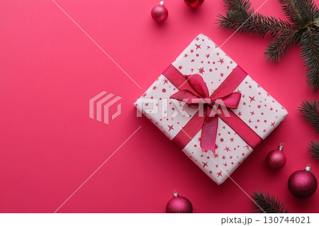 Christmas gift box decorated with ribbon surrounded by fir branches and Christmas baubles on pink background with copy space 130744021