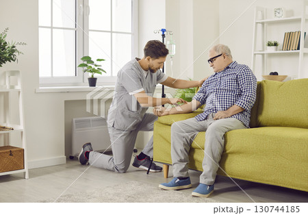 Male caregiver setting up iv drip to senior patient 130744185
