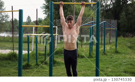 Muscular athlete doing pull ups on horizontal bar at sports ground. Young shirtless sportsman exercising at nature. Strong sporty man training outdoor. Concept of healthy and active lifestyle. Slow mo Muscular athlete doing pull ups on horizontal bar at sports ground. Young shirtless sportsman exercising at nature. Strong sporty man training outdoor. Concept of healthy and active lifestyle. Slow mo 130745330