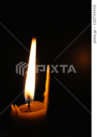 One waxy candle burns in the dark casting a red glow. Concept photo for mournful occasion One waxy candle burns in the dark casting a red glow. Concept photo for mournful occasion 130745410
