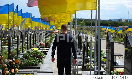 Mourning man go among countless graves of ukrainian soldiers with national flags at military cemetery in Kharkiv. Scene reflects personal sorrow and nation collective loss caused by russian aggression Mourning man go among countless graves of ukrainian soldiers with national flags at military cemetery in Kharkiv. Scene reflects personal sorrow and nation collective loss caused by russian aggression 130745418