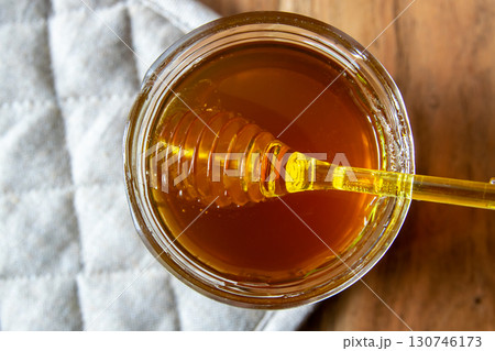 Honey big glass jar with honeycomb and yellow spoon stay on the wood table with rustic napkin. 130746173