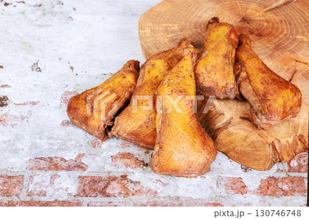 Five crispy chicken legs sit on wooden cutting board surrounded by weathered stone surface 130746748
