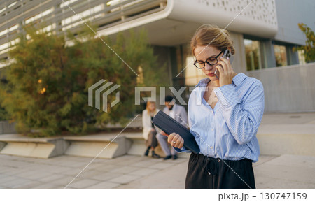 A businesswoman engaged in using her smartphone while situated in a bustling urban setting 130747159
