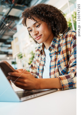 A young woman interacts with technology in a modern workspace, enjoying a cheerful atmosphere 130747165