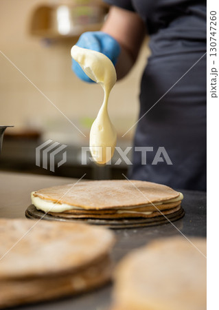 Pastry chef spreading cream on cake layer in professional bakery kitchen, close-up Pastry chef spreading cream on cake layer in professional bakery kitchen, close-up 130747260
