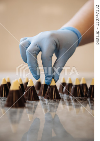 Chocolate cones with white tips being arranged by hand in a professional candy kitchen 130747332