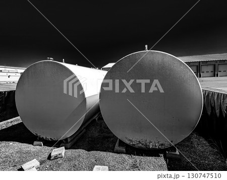 Large industrial storage tanks placed side by side in an outdoor facility under clear blue sky during daytime hours 130747510