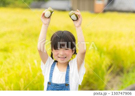 田んぼの前でおにぎりを食べる女の子 130747906