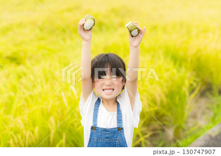 田んぼの前でおにぎりを食べる女の子 130747907