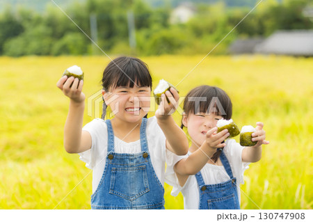 田んぼの前でおにぎりを持つ姉妹 130747908