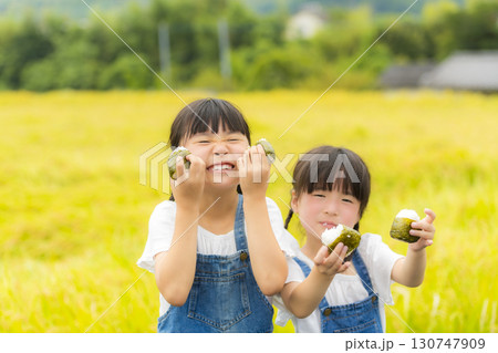 田んぼの前でおにぎりを持つ姉妹 130747909