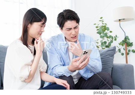困った表情でスマートフォンを見る男女 130749333