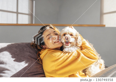 Cheerful Woman Hugging Fluffy Dog on a Couch. 130749358