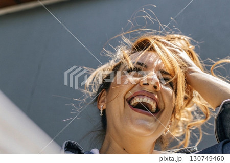 Woman laughing with hand in hair under bright sunlight. 130749460