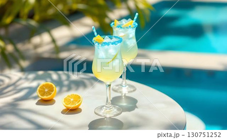 Two glasses of lemonade with straws and lemon slices sit on a table near a pool, ideal for a summer pool party Two glasses of lemonade with straws and lemon slices sit on a table near a pool, ideal for a summer pool party 130751252