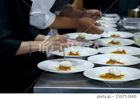 chefs in a professional kitchen garnishing dessert plates with precision. restaurant chef team showcasing fine dining presentation, culinary creativity, and teamwork in food preparation. 130751660
