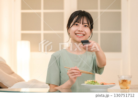 夕食を食べながらテレビのリモコンを操作する若いアジア人女性 夕食を食べながらテレビのリモコンを操作する若いアジア人女性 130751712