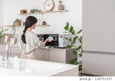 キッチンで電子レンジを使う女性(オーブンレンジ,温める) キッチンで電子レンジを使う女性(オーブンレンジ,温める) 130753357