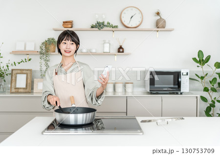 キッチンでスマホを見ながら料理するエプロン姿の若いアジア人女性 キッチンでスマホを見ながら料理するエプロン姿の若いアジア人女性 130753709