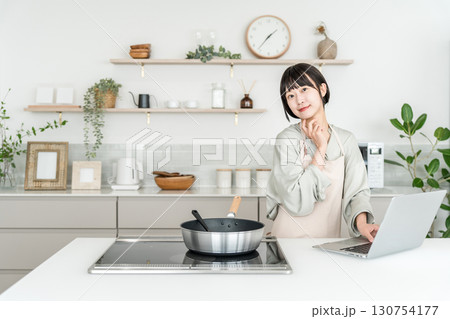 キッチンでパソコンを見ながら料理するエプロン姿の若いアジア人女性 130754177