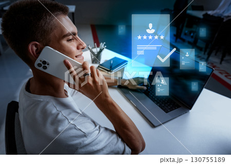 Young professional engaged in remote work while on a phone call, showcasing digital communication and productivity tools Young professional engaged in remote work while on a phone call, showcasing digital communication and productivity tools 130755189