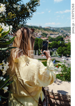 Young woman taking a smartphone picture of a scenic view with flowers in the foreground Young woman taking a smartphone picture of a scenic view with flowers in the foreground 130755268