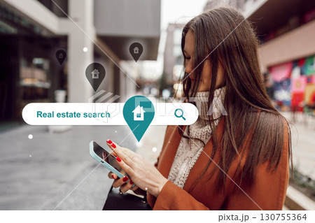 Woman using smartphone for real estate search in urban setting during daytime 130755364