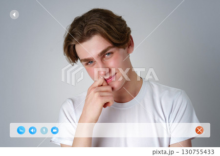 Young man smiles playfully while resting his chin on his hand against a neutral background 130755433