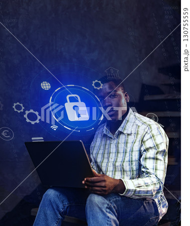 Young man working on cybersecurity project while seated with laptop in a dimly lit space 130755559