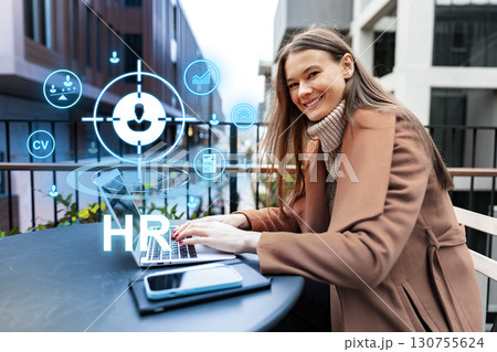 Professional woman working on laptop outdoors with HR icons displayed, showcasing modern recruitment technology Professional woman working on laptop outdoors with HR icons displayed, showcasing modern recruitment technology 130755624