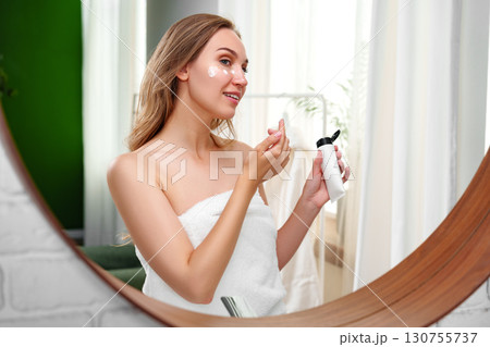 Woman applying skincare product in a bright bathroom during morning routine 130755737