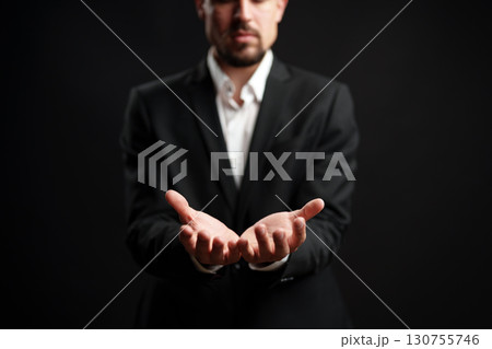 Businessman presenting hands forward in professional attire against a dark background while delivering a confident impression 130755746