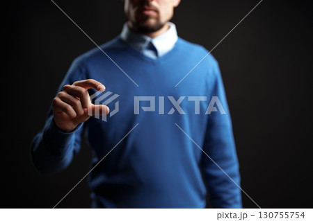 Person in blue sweater using hand gesture to symbolize measurement against dark background 130755754
