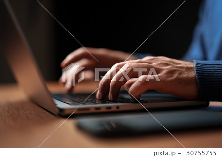 Hands typing on a laptop in a dimly lit workspace during evening hours 130755755